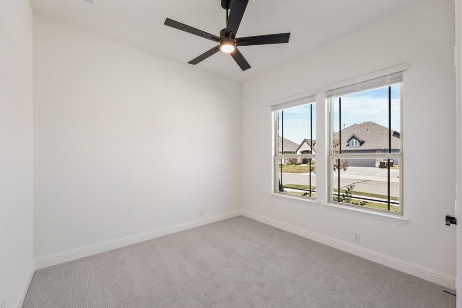 Empty bedroom with gray carpet, black ceiling fan, and two windows overlooking a neighborhood street. Empty bedroom with gray carpet, black ceiling fan, and two windows overlooking a neighborhood street.