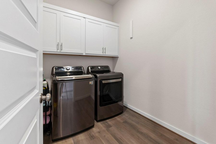 Dedicated laundry room featuring white shaker cabinetry with brushed nickel hardware, wood-finish flooring, and white baseboards