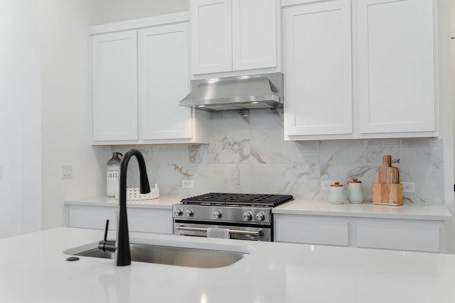 Modern and clean look kitchen featuring white cabinetry, stainless steel range with gas cooktop, tasteful backsplash, exhaust hood, and light stone counters