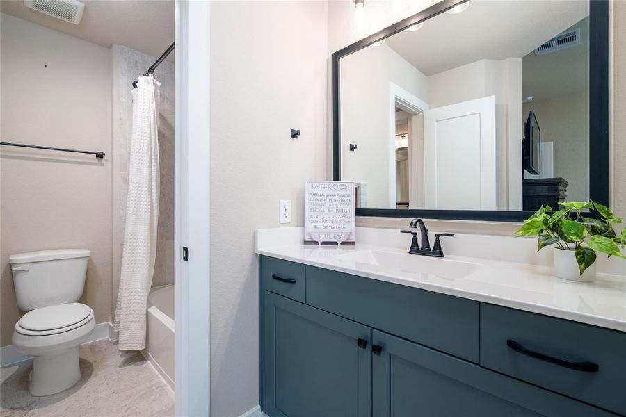 This bedroom’s private sink area showcases a custom-painted vanity with a framed mirror, that conveniently connects to a shared bathroom featuring a shower/tub combo and toilet, providing comfort and ease for daily living. This bedroom’s private sink area showcases a custom-painted vanity with a framed mirror, that conveniently connects to a shared bathroom featuring a shower/tub combo and toilet, providing comfort and ease for daily living.