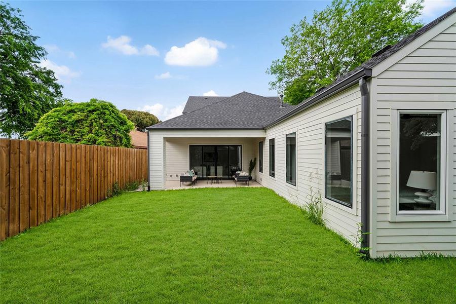 The property features a spacious lawn, a wooden fence, and a covered patio area
