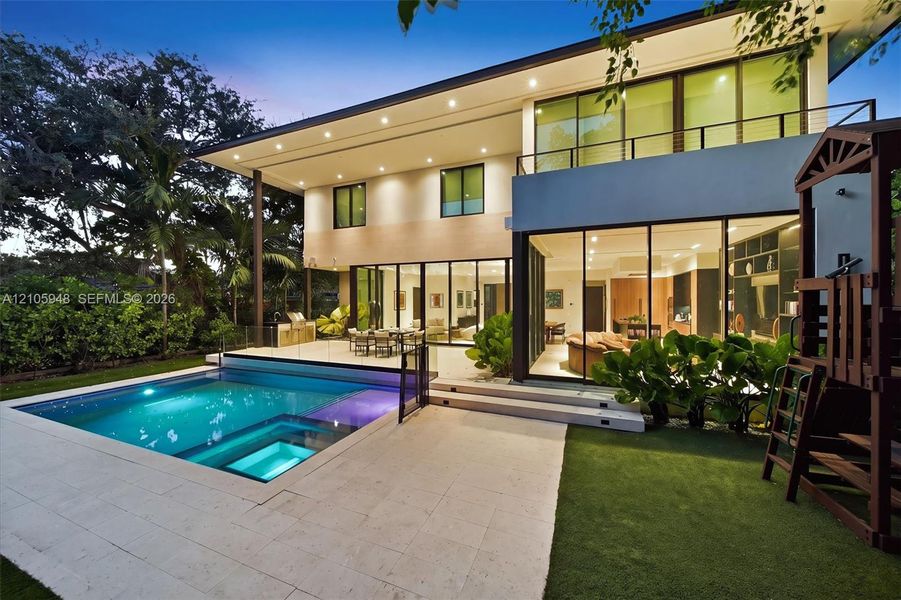 Modern residence featuring floor-to-ceiling glass sliding doors, a two-story balcony with metal railings, a paved stone pool deck, and a recessed swimming pool