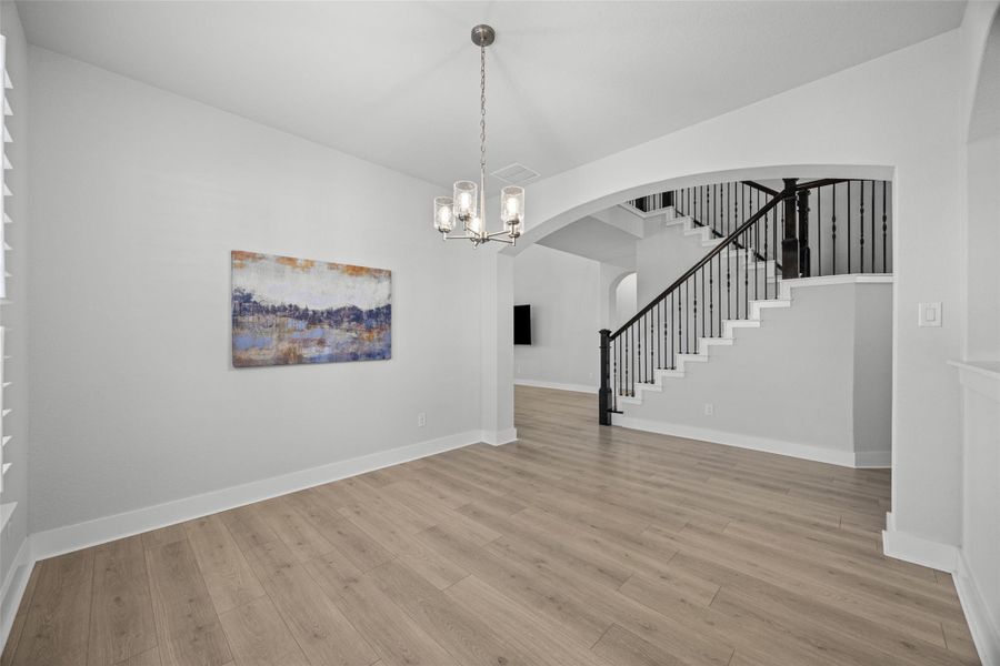 A well-lit dining area features light wood flooring and a classic chandelier, offering a seamless flow to the adjacent staircase with elegant iron balusters.