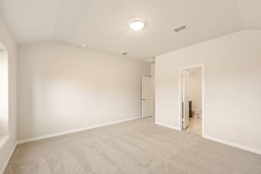 Empty bedroom with beige carpet, white walls, and an open ensuite bathroom door