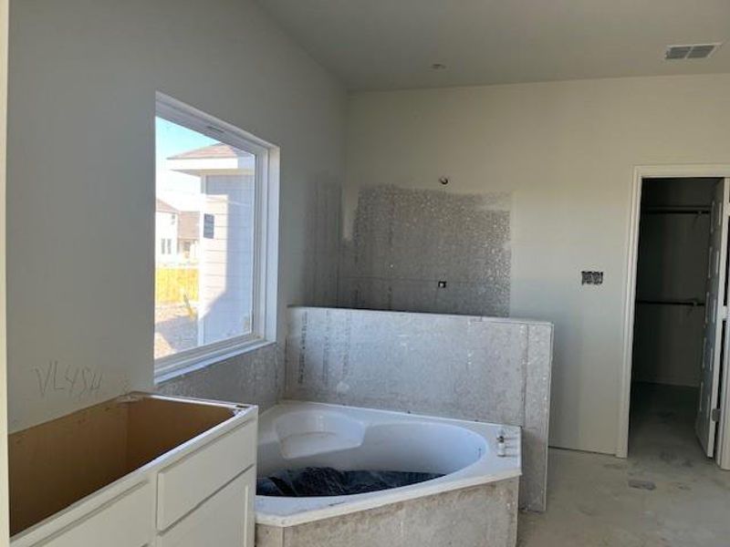 Full bath with unfinished concrete flooring, a walk in closet, visible vents, and a garden tub