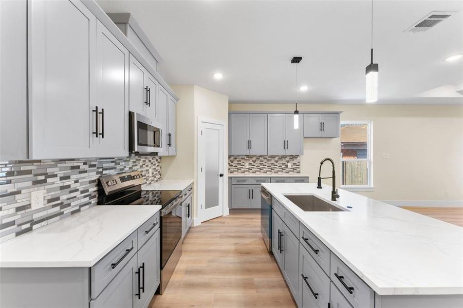 Kitchen featuring appliances with stainless steel finishes, pendant lighting, sink, a kitchen island with sink, and light stone counters