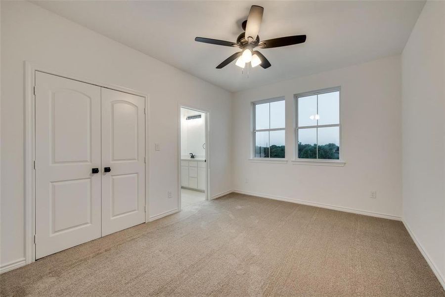 Unfurnished bedroom featuring light colored carpet, ensuite bathroom, ceiling fan, and a closet