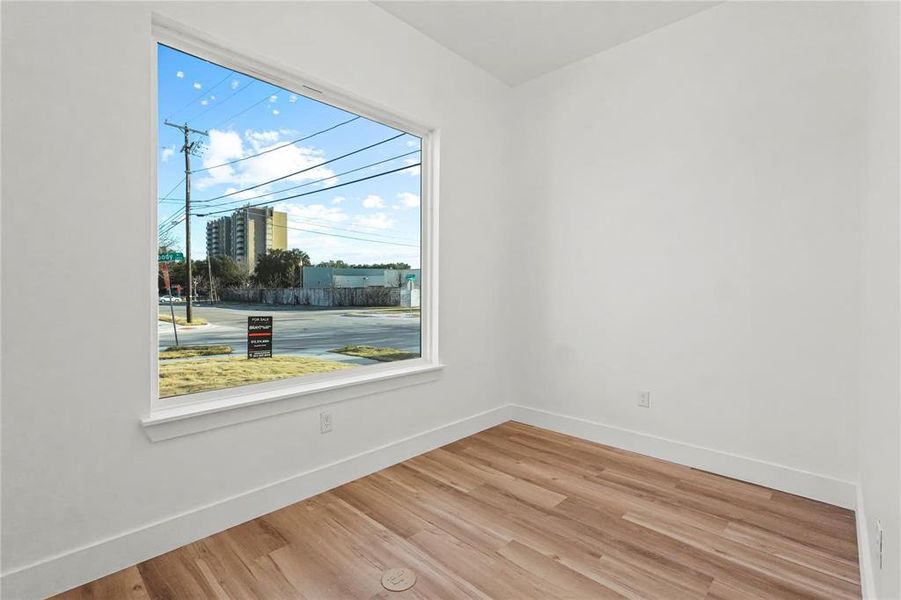 Bright room featuring a large picture window, wood-finish flooring, crisp white walls, and substantial baseboards