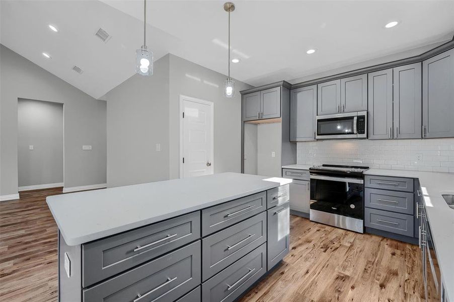 Kitchen featuring gray cabinetry, a center island, light hardwood / wood-style flooring, vaulted ceiling, and appliances with stainless steel finishes