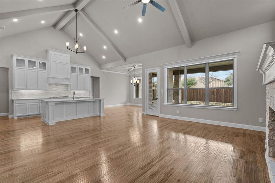 Unfurnished living room with light wood-type flooring, ceiling fan with notable chandelier, a fireplace, and beam ceiling. Not actual home. Previous built example.