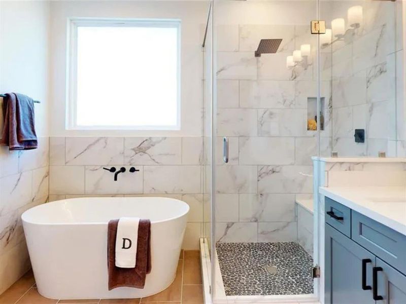 A modern bathroom with a white bathtub, a walk-in shower, and a vanity. The bathroom has white subway tiles with gray veining throughout. The walls are a light cream color, and the lighting is bright. There is a window above the bathtub, letting in natural light.