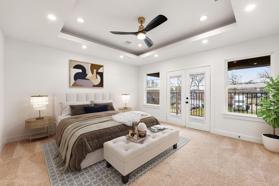 Spacious primary bedroom featuring a tray ceiling with recessed lighting and ceiling fan, plush carpeting, and abundant natural light. French doors lead to a private balcony, creating a relaxing retreat with an airy, upscale feel.