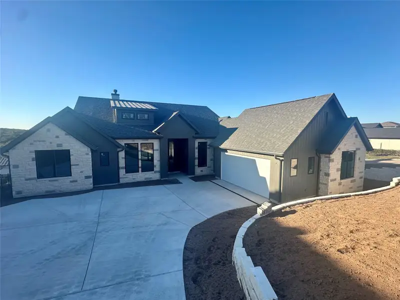 View of front of home featuring concrete driveway, stone siding, a garage, and a shingled roof View of front of home featuring concrete driveway, stone siding, a garage, and a shingled roof