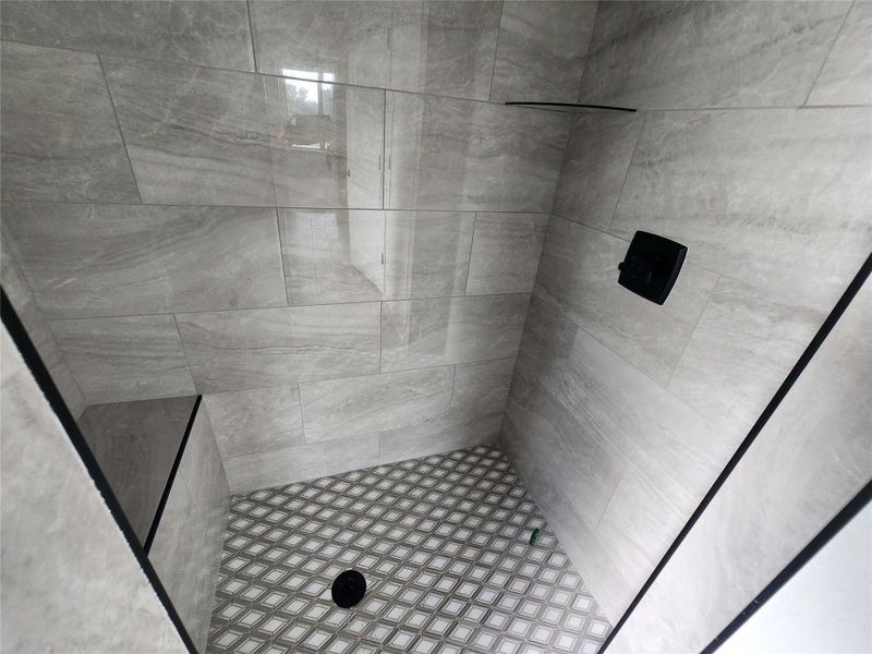 Walk-in shower featuring light gray rectangular wall tiles, a built-in bench, and a geometric pattern floor tile