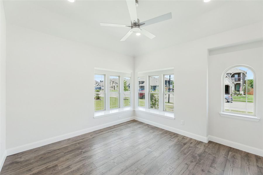 Empty room with vaulted ceiling, ceiling fan, hardwood floors, and large corner windows with arched accent window Empty room with vaulted ceiling, ceiling fan, hardwood floors, and large corner windows with arched accent window