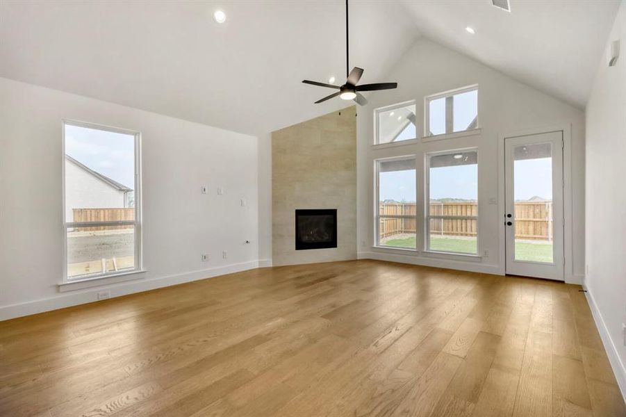 Unfurnished living room with a high ceiling, light wood-style flooring, a large fireplace, a ceiling fan, and recessed lighting