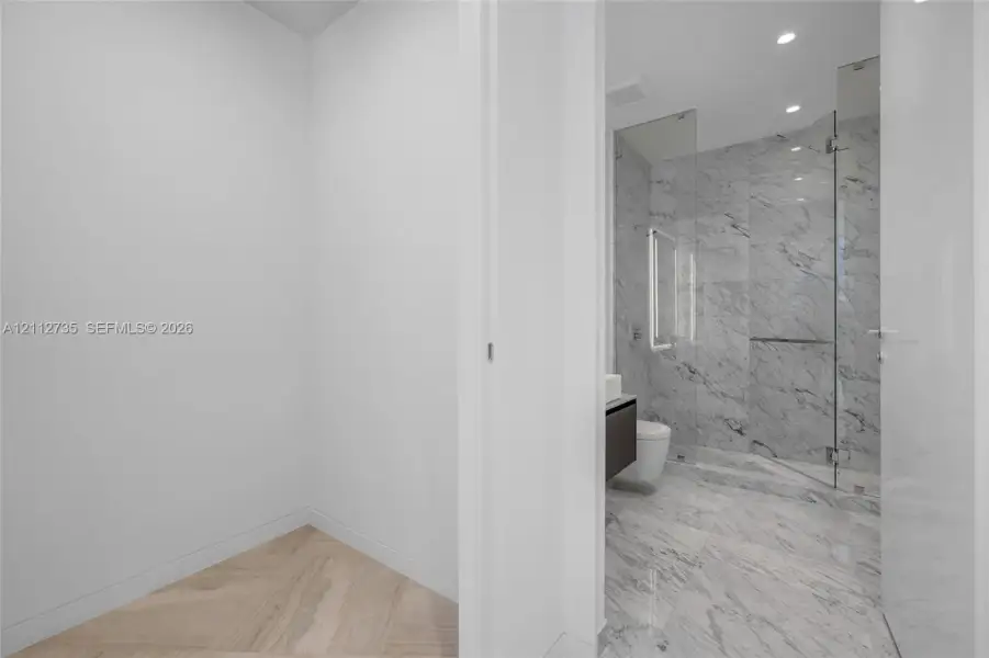 Bathroom featuring stone-finish wall and floor tile, glass-enclosed shower, wall-mounted cabinetry, and a wood-finish herringbone floor