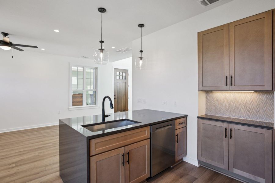 Kitchen featuring a peninsula, dark wood finished floors, dark stone countertops, pendant lighting, and stainless steel dishwasher