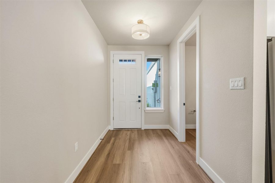 Bright entryway featuring light wood flooring, neutral wall colors, and modern light fixture. A side door leads to powder bathroom.