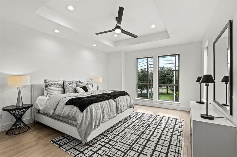 Bedroom with wood-type flooring, ceiling fan, and a tray ceiling