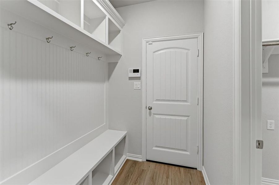 Dedicated mudroom area featuring a built-in bench with storage cubbies, beadboard paneling, coat hooks, upper shelving, and wood-finish flooring Dedicated mudroom area featuring a built-in bench with storage cubbies, beadboard paneling, coat hooks, upper shelving, and wood-finish flooring