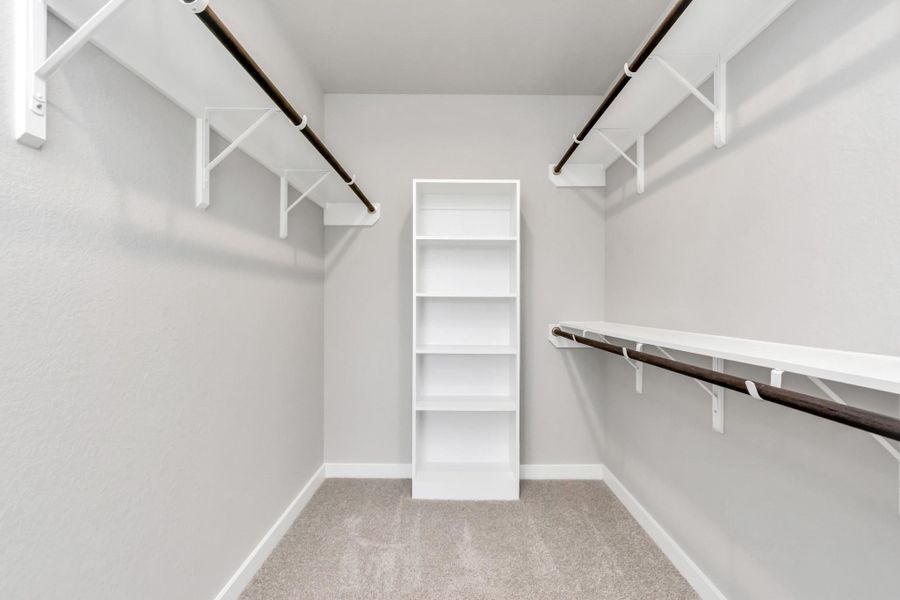Experience luxury in this spacious walk-in closet with high ceilings and plush carpet. Warm paint tones, built-in shelving, recessed lighting, and dark finishes create a contemporary and functional retreat. Sample photo of completed plan. As-built color and selections may vary. Experience luxury in this spacious walk-in closet with high ceilings and plush carpet. Warm paint tones, built-in shelving, recessed lighting, and dark finishes create a contemporary and functional retreat. Sample photo of completed plan. As-built color and selections may vary.