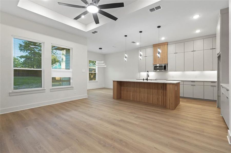 Kitchen featuring modern cabinets, brown cabinetry, pendant lighting, an island with sink, and light wood-type flooring