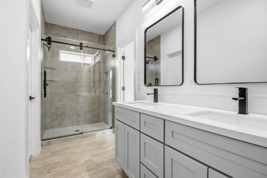 Sleek modern primary bathroom featuring a spacious glass-enclosed shower, dual sinks with elegant fixtures, and ample storage with stylish cabinetry.