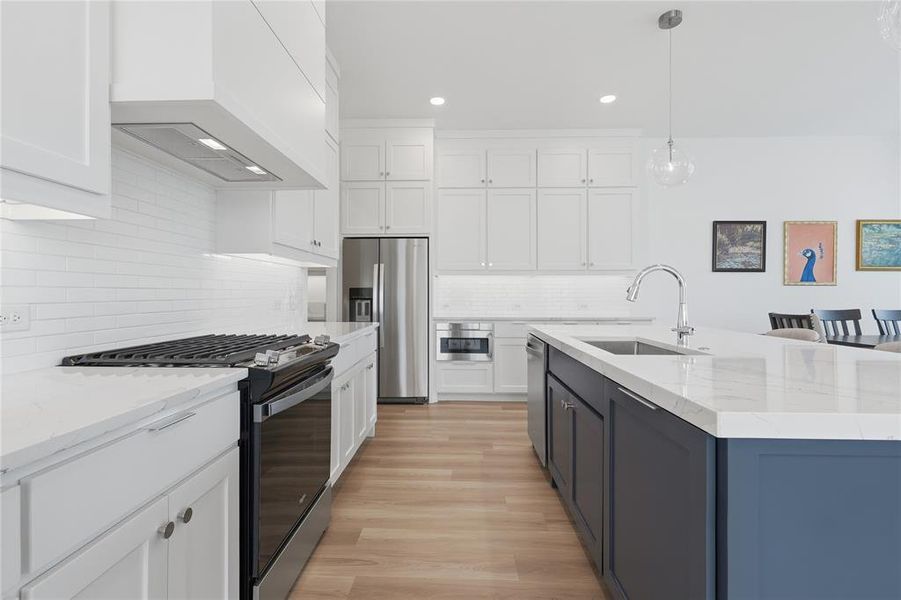 Modern kitchen featuring white shaker cabinetry, stainless steel appliances, white subway tile backsplash, light wood-finish flooring, and a contrasting blue-gray island with a single-basin sink