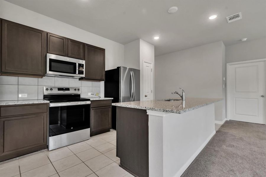 A well-appointed kitchen features a central island, granite countertops, and stainless steel appliances.