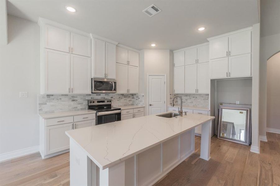 Kitchen with sink, white cabinetry, an island with sink, and appliances with stainless steel finishes