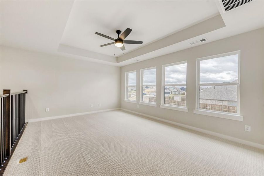 Unfurnished room featuring a ceiling fan, light carpet, and a tray ceiling