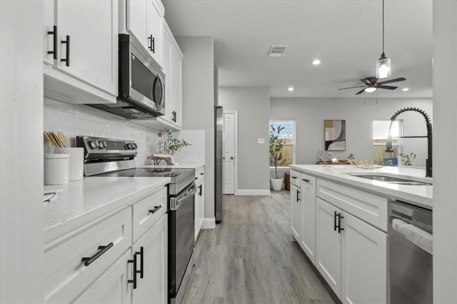 Kitchen with white cabinetry, sink, ceiling fan, hanging light fixtures, and appliances with stainless steel finishes