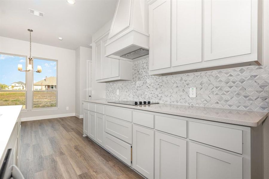 Kitchen featuring hanging light fixtures, white cabinetry, a chandelier, backsplash, and light wood-type flooring