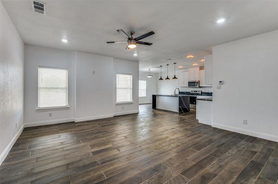 Unfurnished living room featuring ceiling fan and dark wood-style flooring Unfurnished living room featuring ceiling fan and dark wood-style flooring