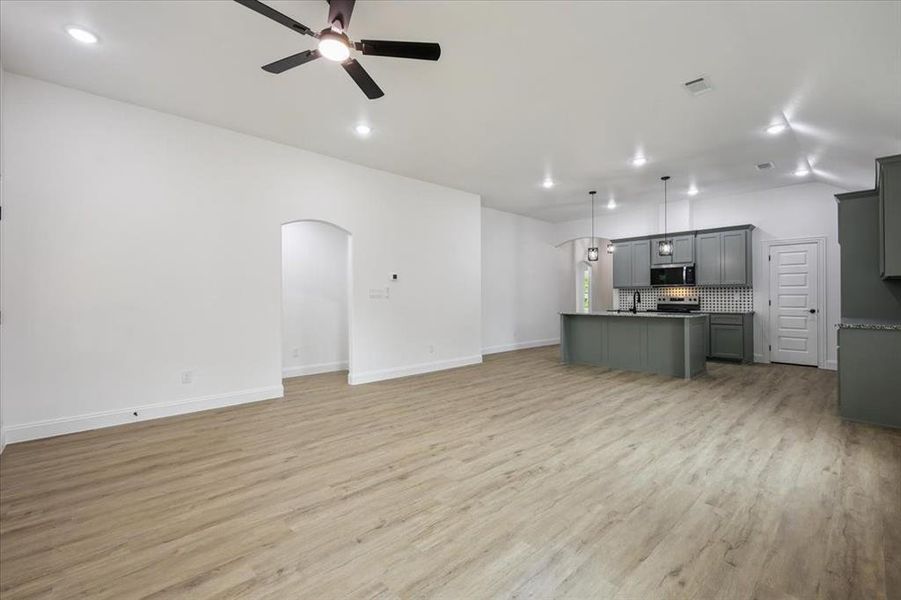 Unfurnished living room with light wood-style flooring, arched walkways, ceiling fan, and recessed lighting Unfurnished living room with light wood-style flooring, arched walkways, ceiling fan, and recessed lighting