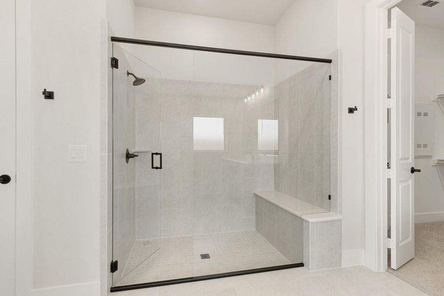 Walk-in shower with glass door, gray tile walls, built-in bench, and black hardware fixtures