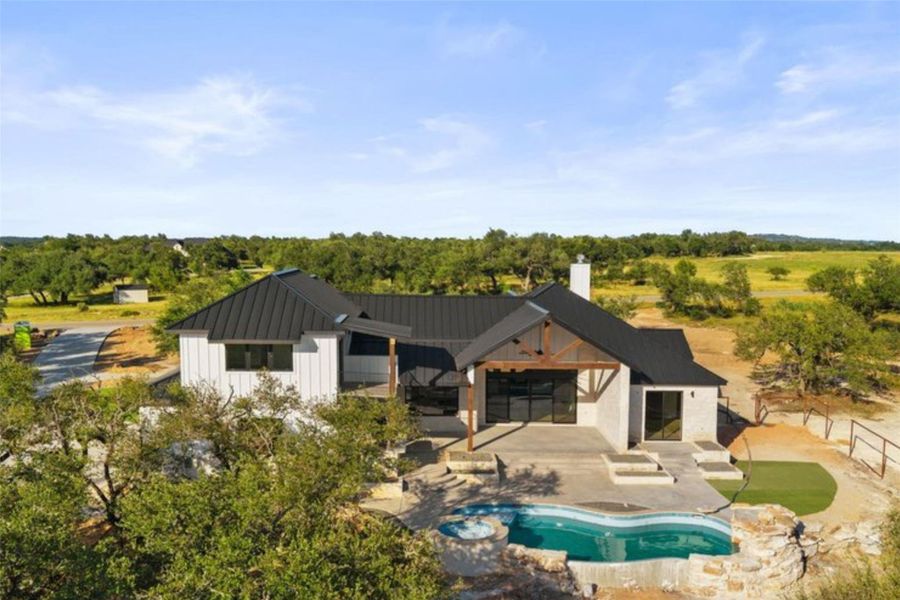 A modern farmhouse-style residence features a sleek black roof, expansive patio, and an inviting pool with a spa. A modern farmhouse-style residence features a sleek black roof, expansive patio, and an inviting pool with a spa.