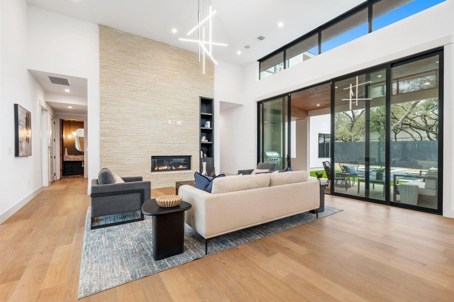 Living room with a high ceiling, recessed lighting, light wood-style flooring, a stone fireplace, and built in features