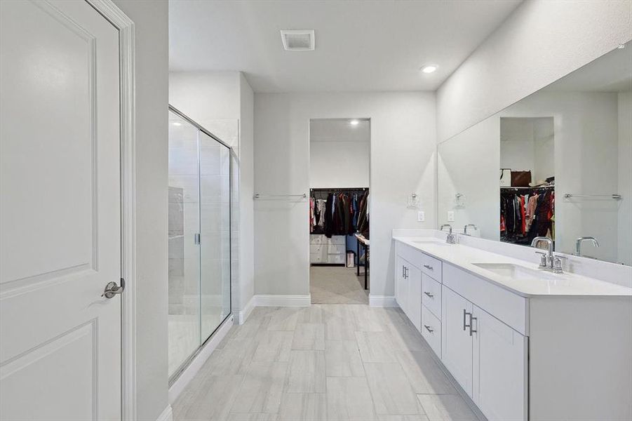 Bathroom with tile floors, a shower with door, vanity with extensive cabinet space, and double sink