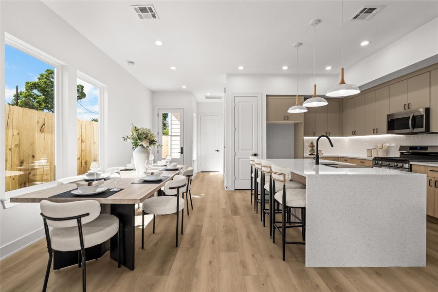 The main floor layout keeps everything open and connected. Light flooring and white walls maximize the natural light throughout the entire space. From the dining area, you have a direct view of the kitchen, which features a breakfast bar with seating and modern pendant lighting.