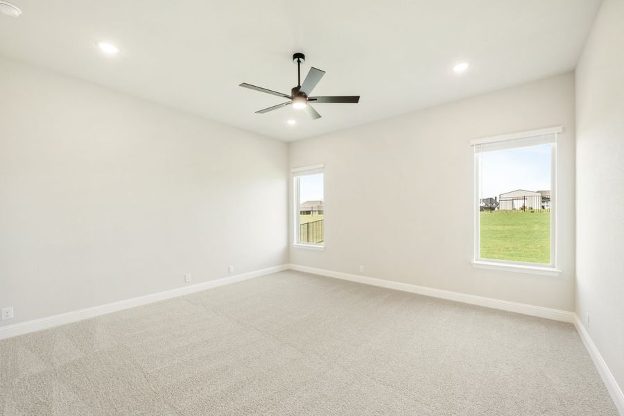 Empty bedroom with carpet flooring, ceiling fan, and two windows overlooking a yard Empty bedroom with carpet flooring, ceiling fan, and two windows overlooking a yard