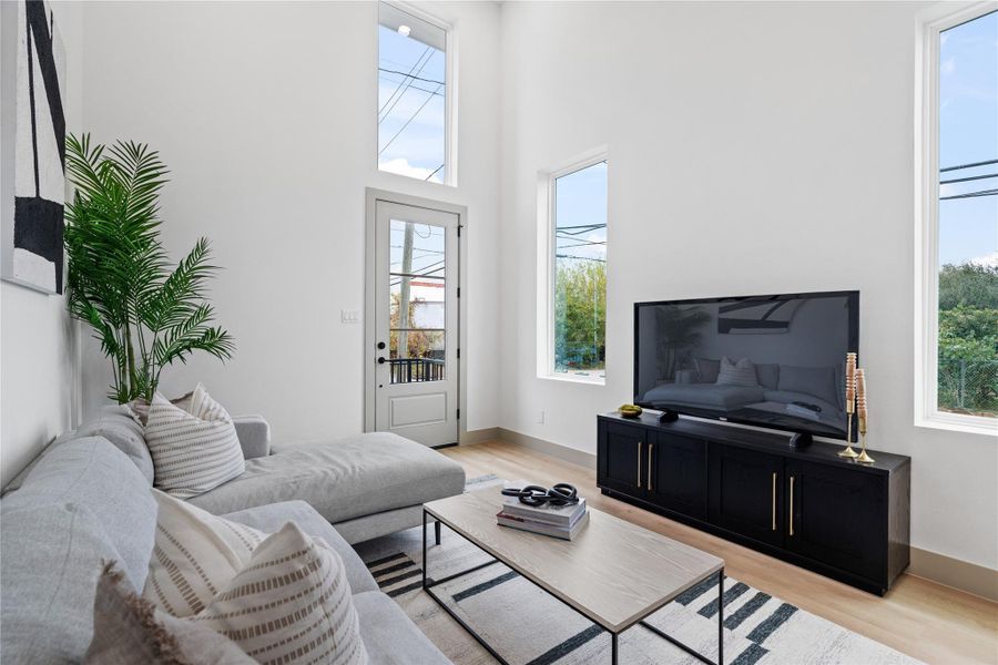 Bathed in natural light from soaring double-height windows, this inviting split-level living room creates a moment of calm and connection, seamlessly overlooked by the elevated kitchen and dining area above. Clean lines, curated textures, and vertical volume bring a modern softness, while thoughtfully placed windows frame treetop views and invite the outdoors in.