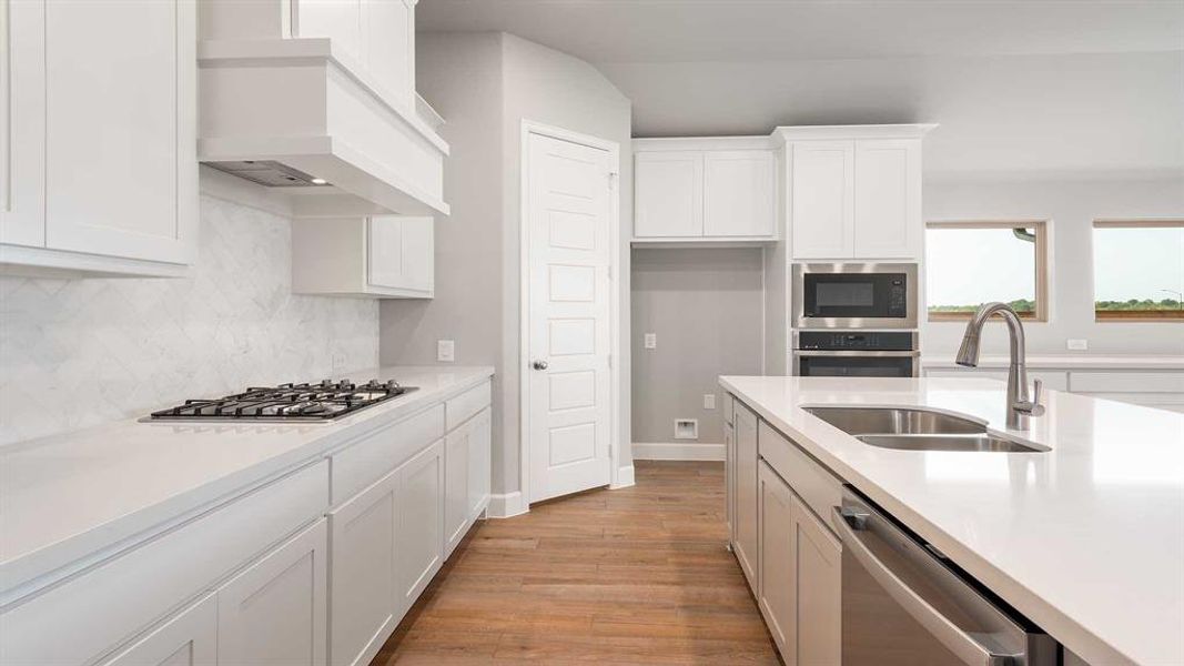 Kitchen with white cabinetry, light hardwood / wood-style flooring, premium range hood, stainless steel appliances, and sink