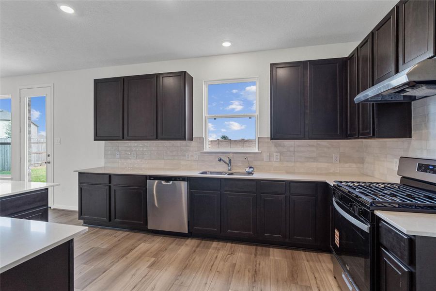 This stunning kitchen boasts high ceilings, recessed lighting, Woodmont Belmont cabinets in Espresso stain, Silestone Linen Cream countertops, stainless steel Whirlpool appliances, a modern Daltile backsplash, an added breakfast bar to kitchen island, and a pantry—all overlooking the expansive Great Room. This stunning kitchen boasts high ceilings, recessed lighting, Woodmont Belmont cabinets in Espresso stain, Silestone Linen Cream countertops, stainless steel Whirlpool appliances, a modern Daltile backsplash, an added breakfast bar to kitchen island, and a pantry—all overlooking the expansive Great Room.