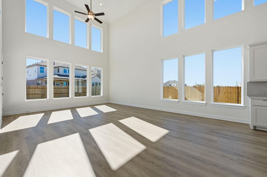 Unfurnished living room featuring dark wood-type flooring, ceiling fan, and a high ceiling