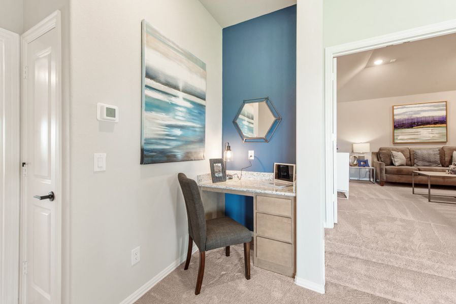 Built-in desk nook with blue accent wall, stone countertop, and gray chair, with living room visible beyond