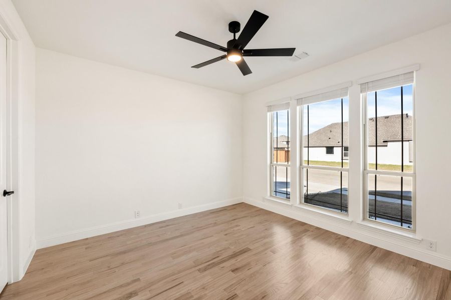 Empty bedroom with light wood floors, black ceiling fan, and three large windows