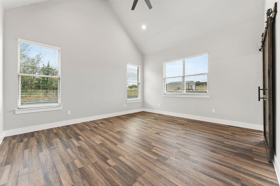 Empty room with ceiling fan, a wealth of natural light, a barn door, and dark hardwood / wood-style floors