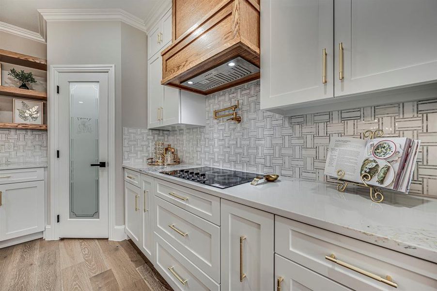 Kitchen with white cabinetry, black electric cooktop, and custom range hood